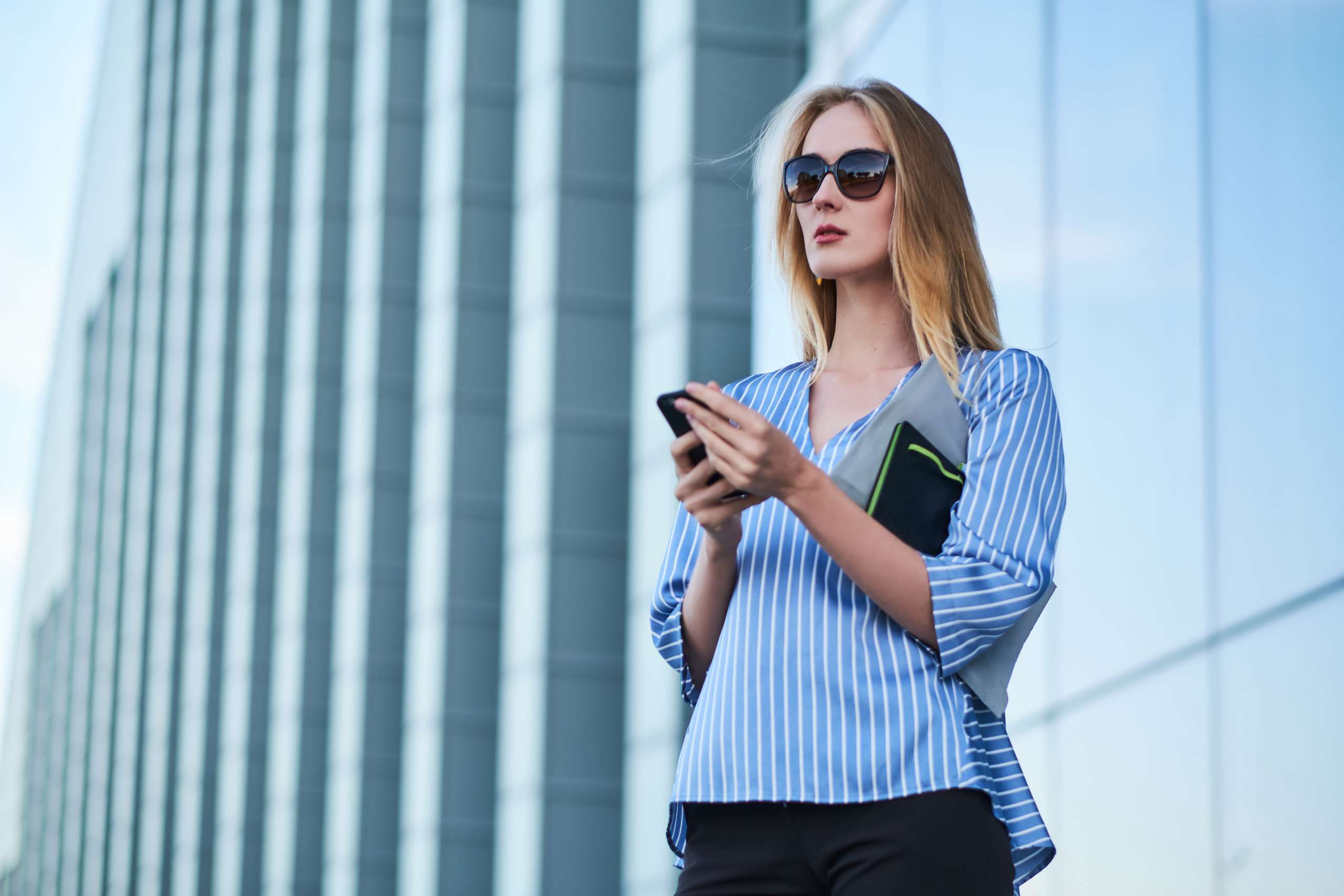 Young successful businesswoman is waiting her new partner on the street with mobile phone in her hands.