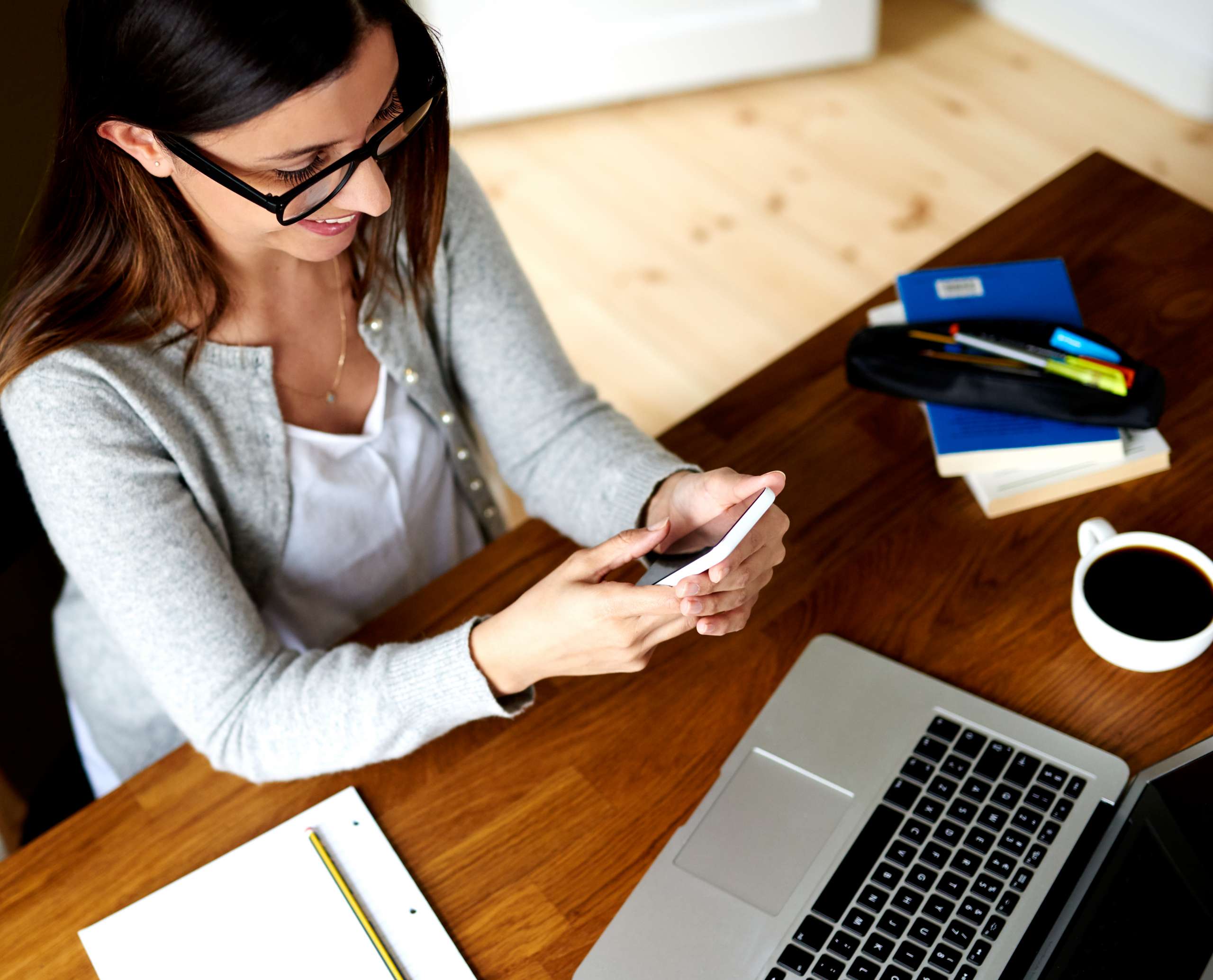 Woman sitting at desk working, smiling and looking at mobile phone.